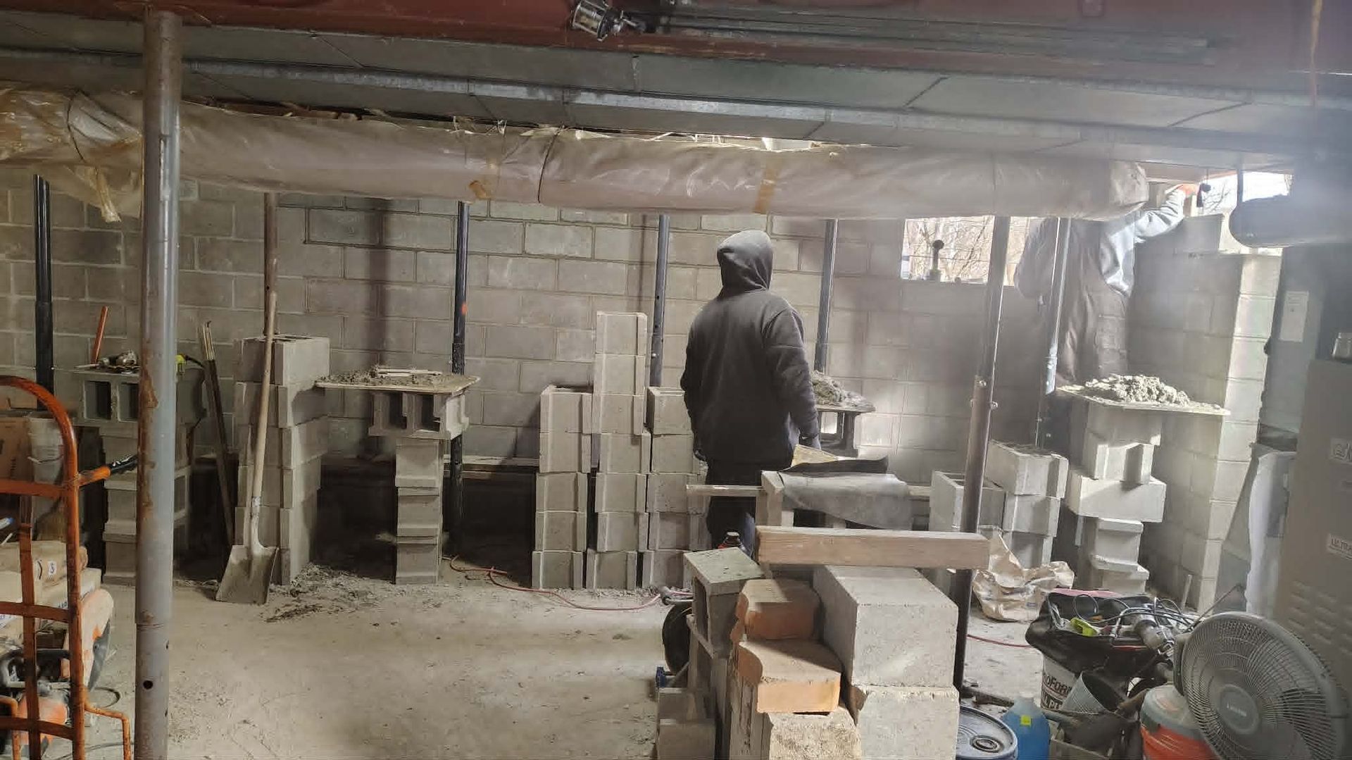 Person in a dusty workshop surrounded by stacked cinder blocks and construction materials.