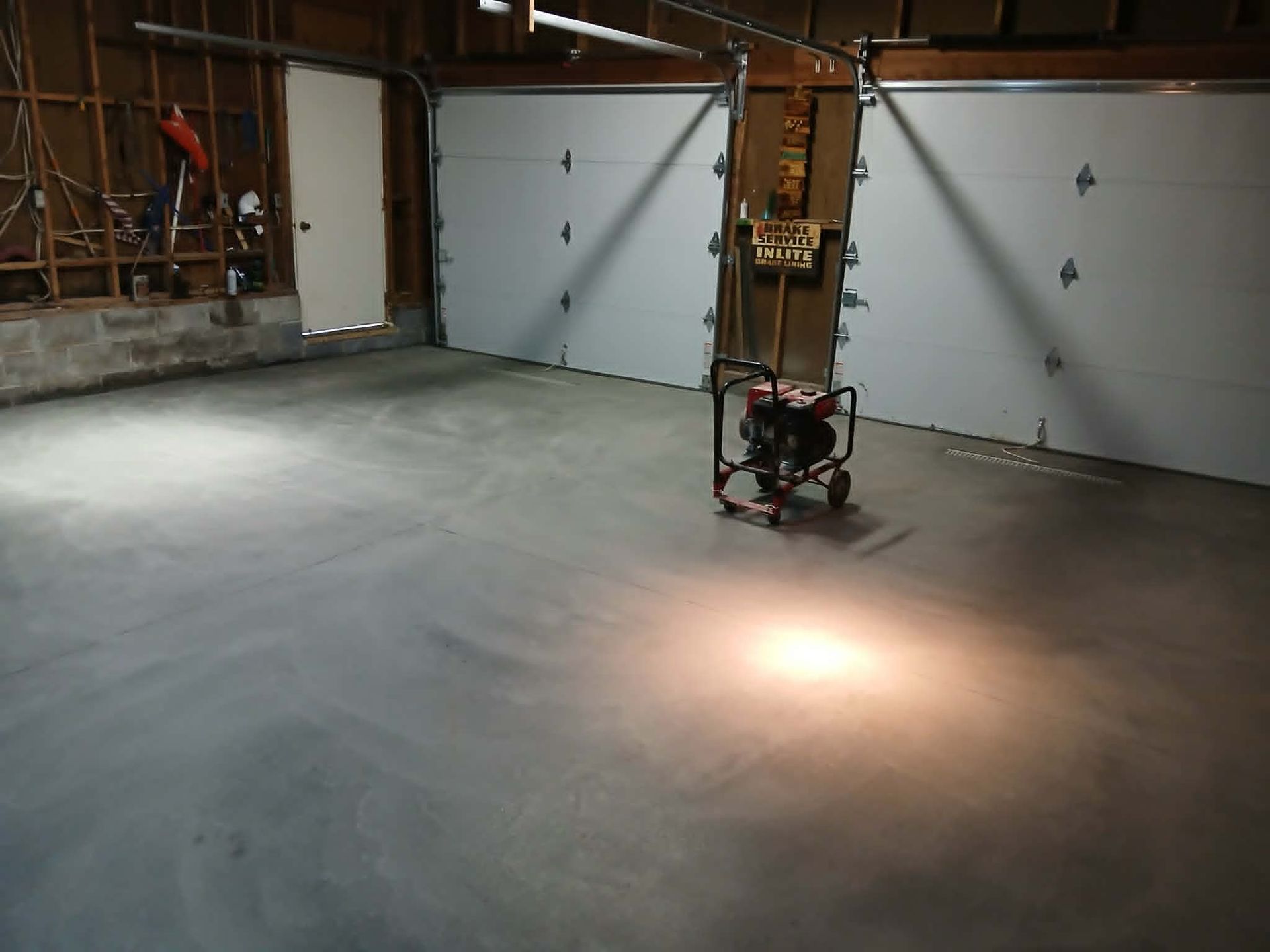 Empty garage with a smooth concrete floor, closed white doors, and a bright light spot near the center.