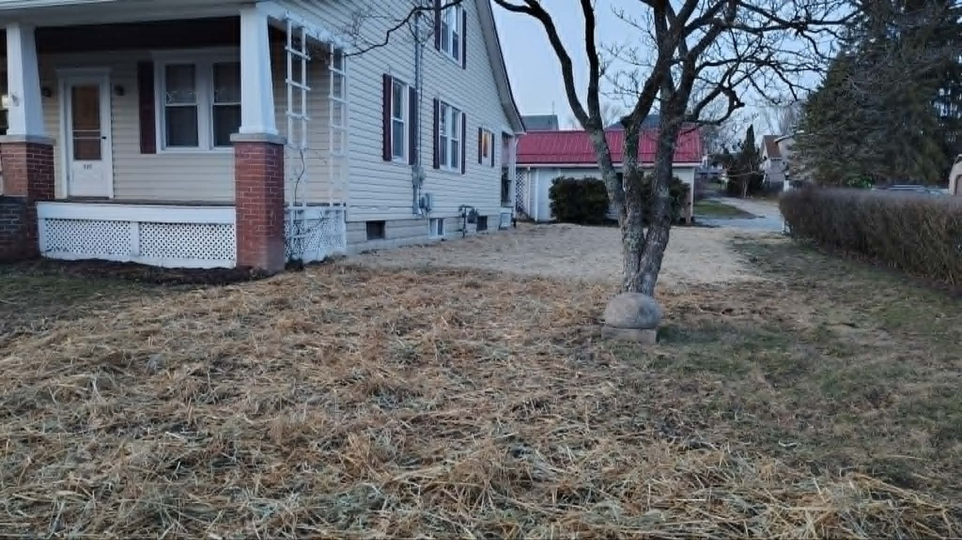 Snow-dusted yard beside a white house with brick columns and a leafless tree under an overcast sky