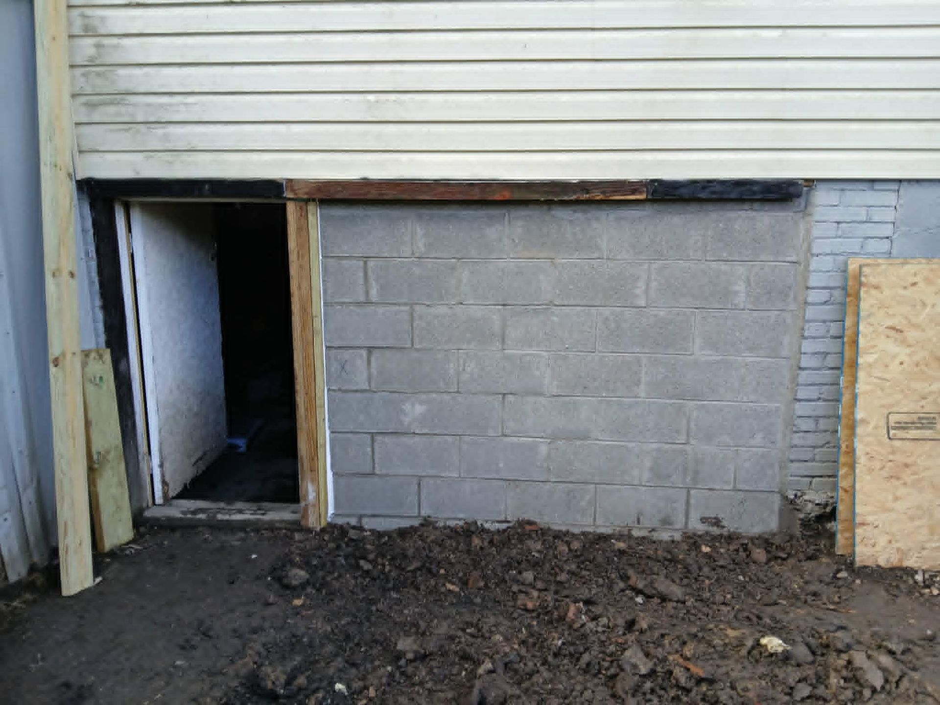 Partially built cinder block wall with open doorway and dirt pile in front