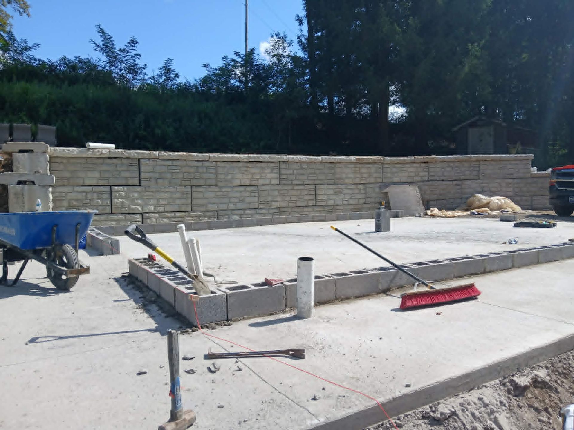 Construction site with concrete foundation slab, stone retaining wall, and tools on a sunny day