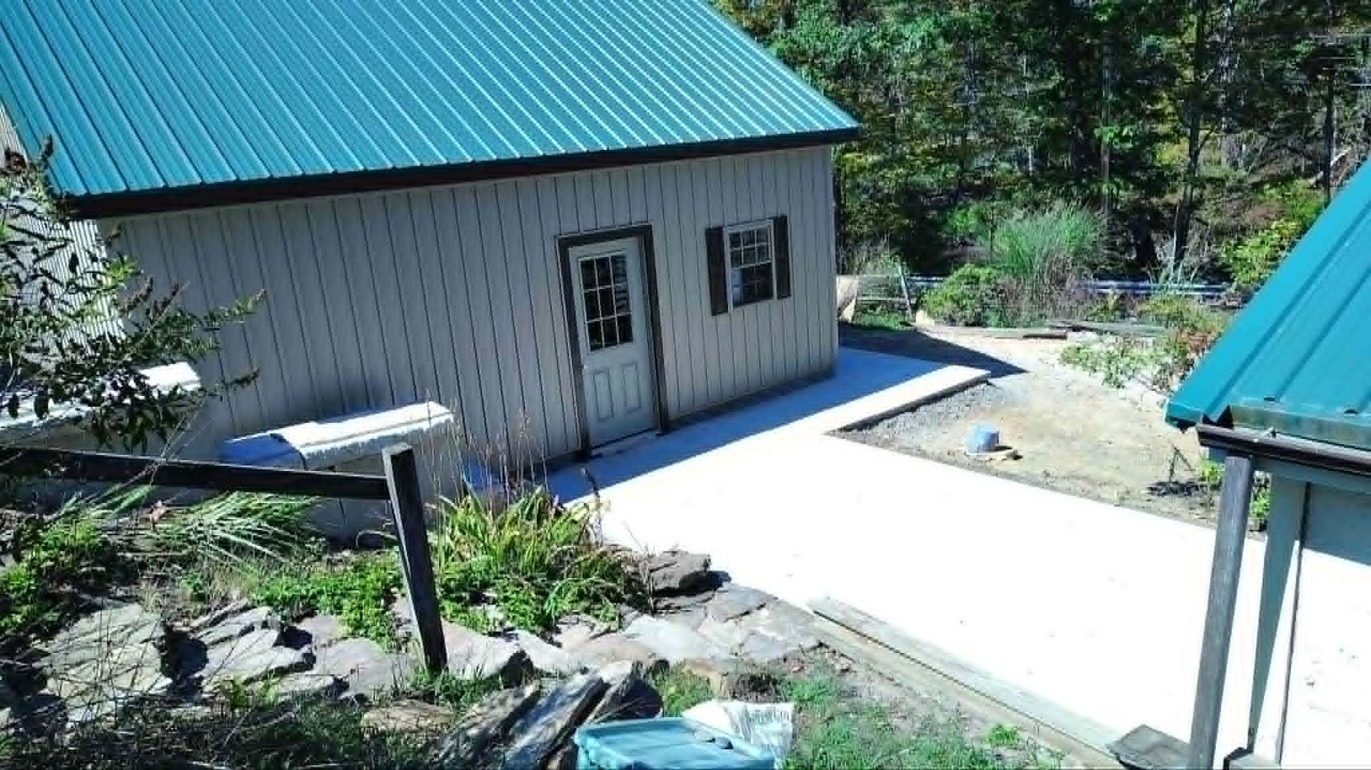Two small buildings with teal roofs beside a white concrete path in a sunny green yard
