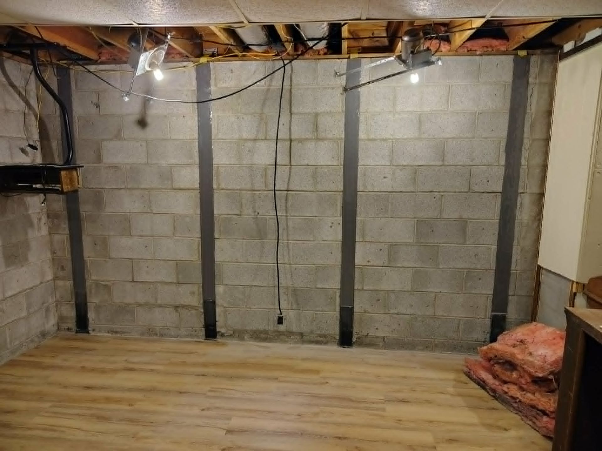 Empty basement with cinder block walls, exposed ceiling joists, and a wood plank floor.