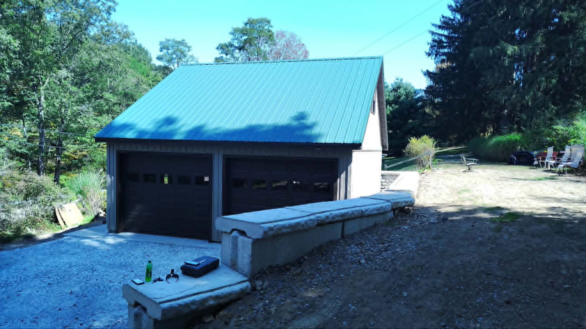 Detached garage with teal roof beside a gravel driveway and trees