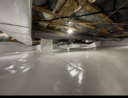 Damaged basement ceiling with exposed pipes and wiring above a wet white floor