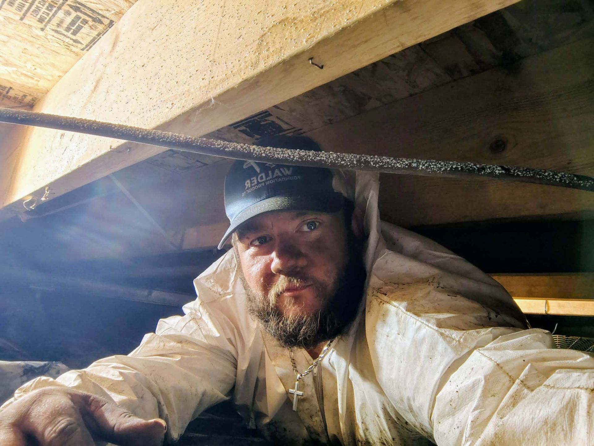 Man in a white jacket crouches under a bridge, looking at the camera with a flashlight nearby.
