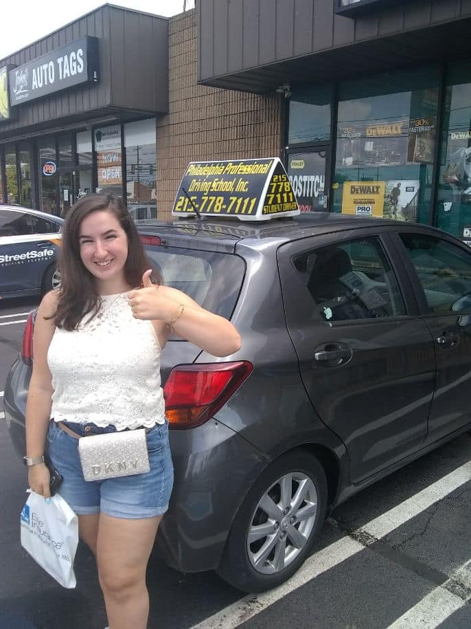 Woman in white top doing ok sign after passing driving school test
