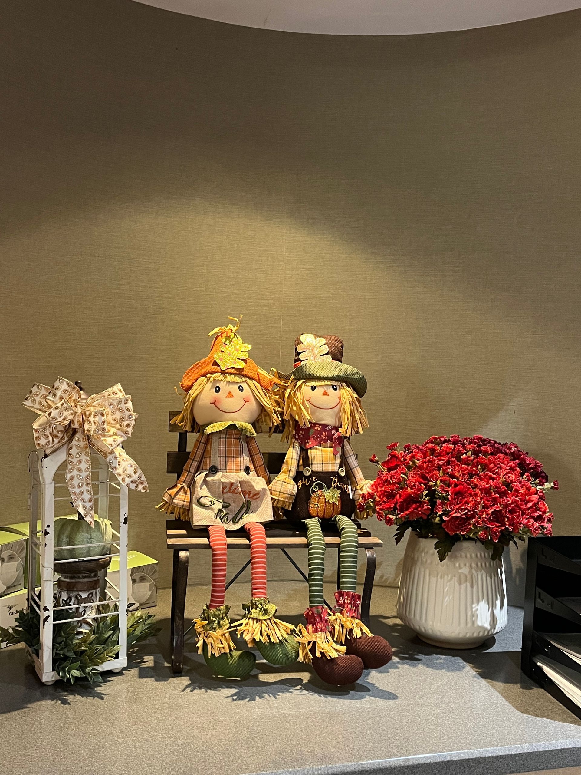 Two scarecrow dolls are sitting on a bench next to a vase of flowers.