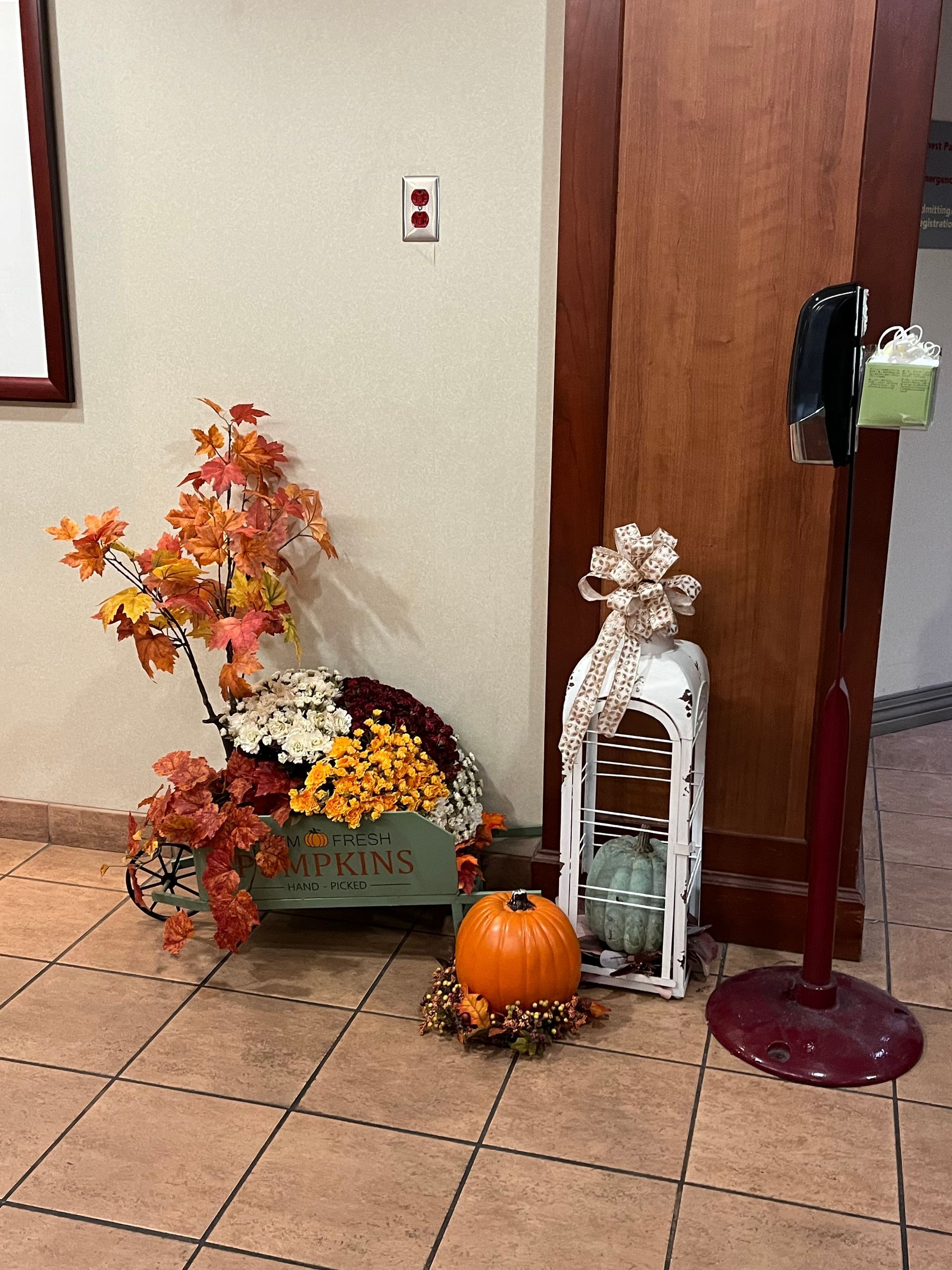 A wagon filled with flowers and pumpkins is in a hallway next to a door.