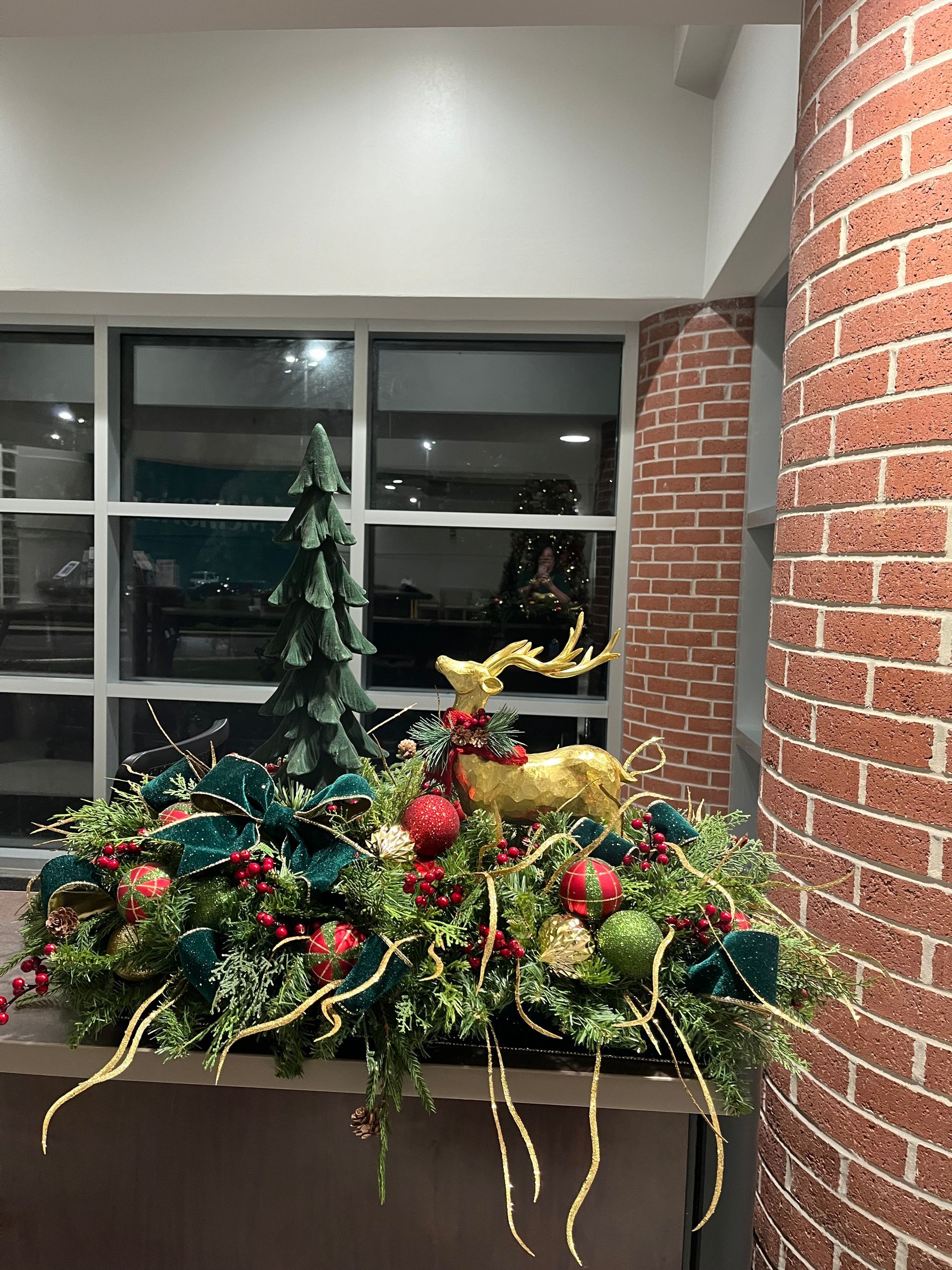 A christmas decoration with a reindeer and a christmas tree in front of a brick wall.
