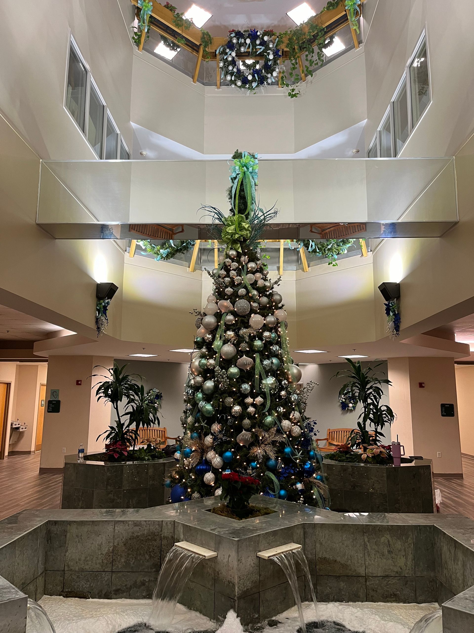 A large christmas tree is in the middle of a building next to a fountain.