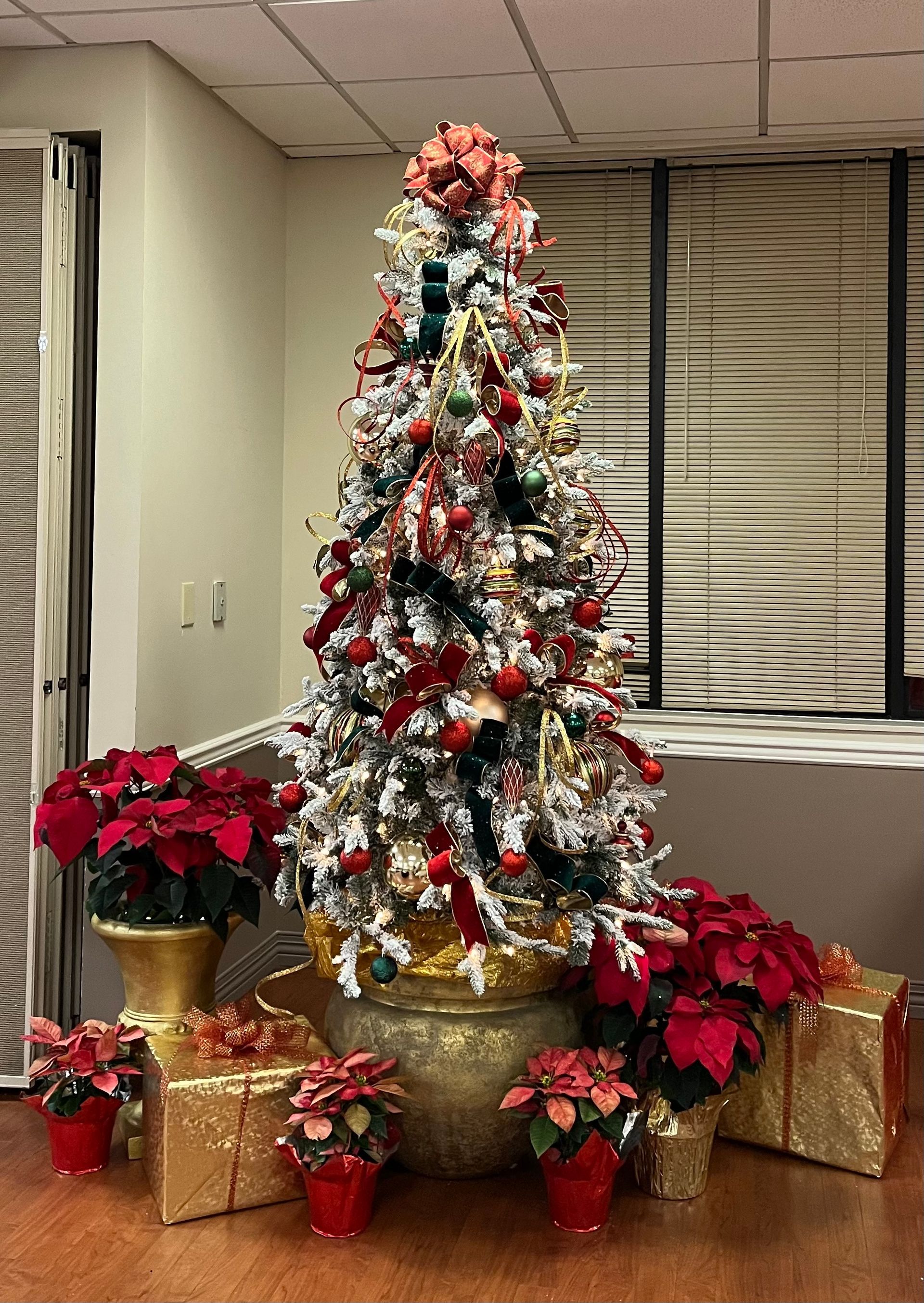 A christmas tree is surrounded by gifts and flowers in a room.