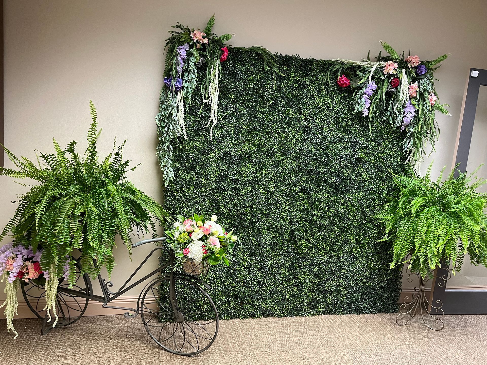 A bicycle is sitting in front of a green wall with flowers and ferns.