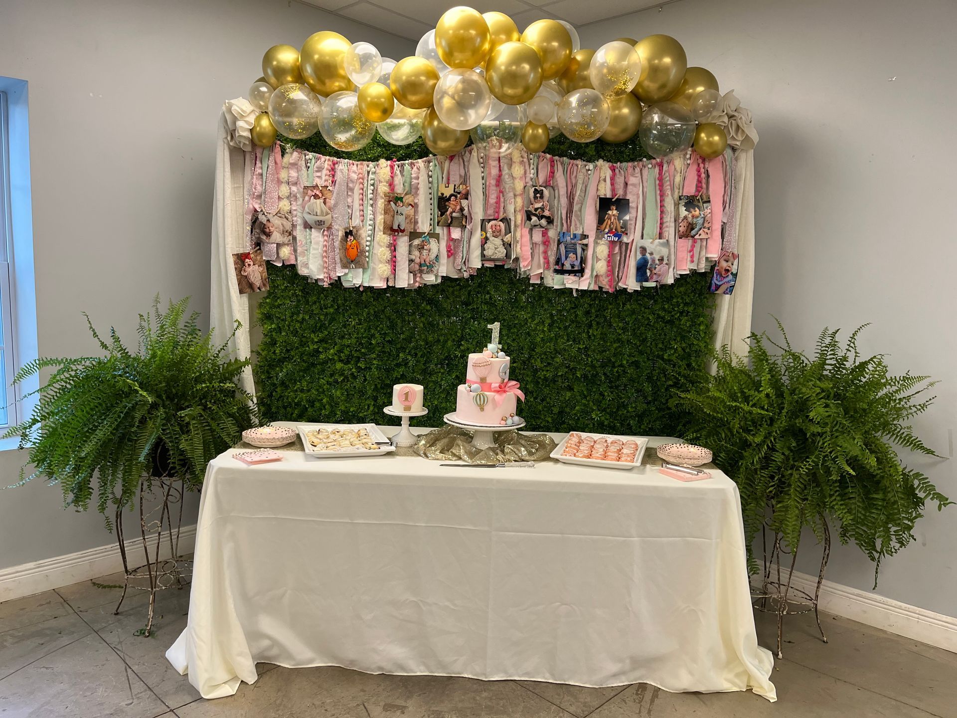A table with a cake and balloons on it in front of a green wall.