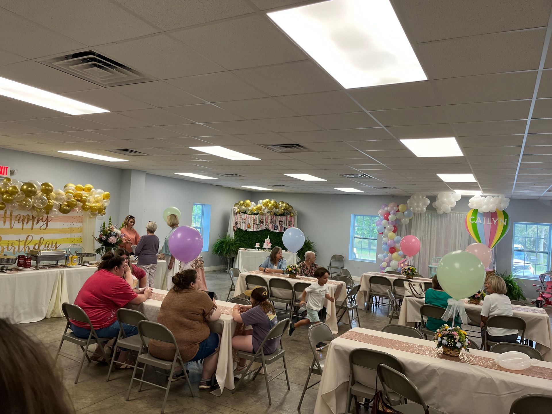 A group of people are sitting at tables in a room decorated with balloons.