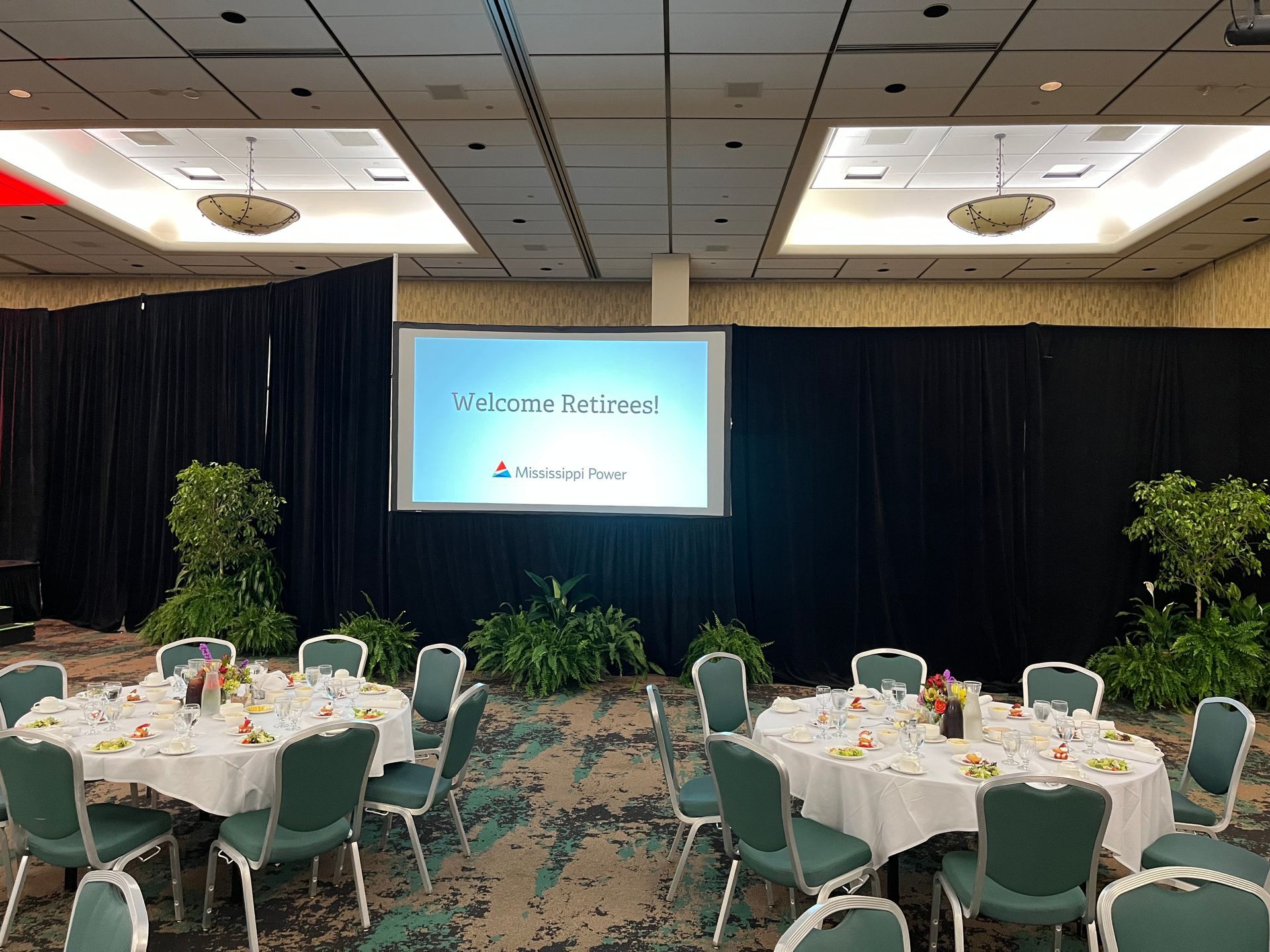 A large room with tables and chairs and a projector screen.