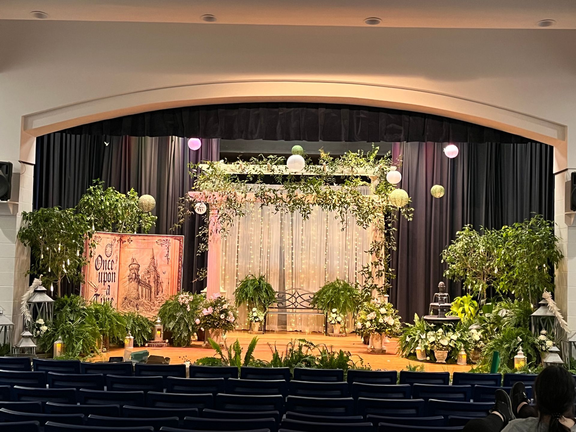 A stage decorated with flowers and plants in an auditorium.