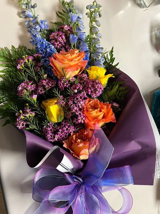 A bouquet of flowers wrapped in purple paper with a purple bow
