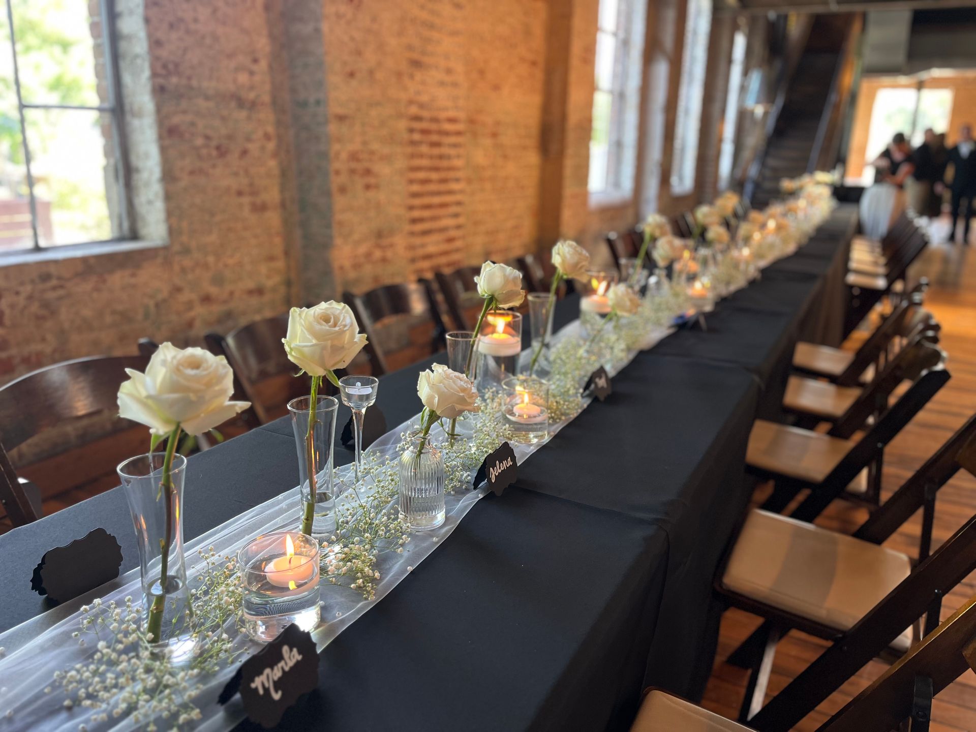 A long table with white roses and candles on it.
