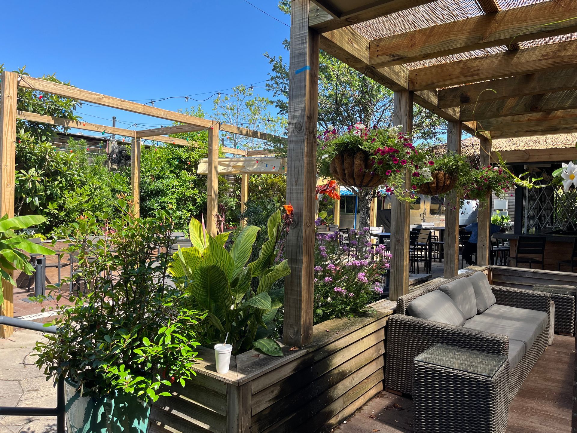 A patio with a couch and chairs under a pergola with hanging baskets of flowers.