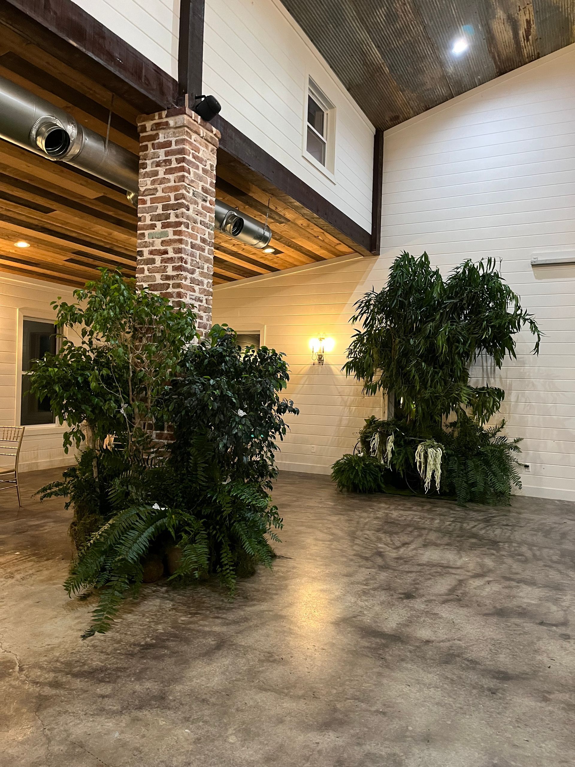 A large room with a brick chimney and lots of plants.