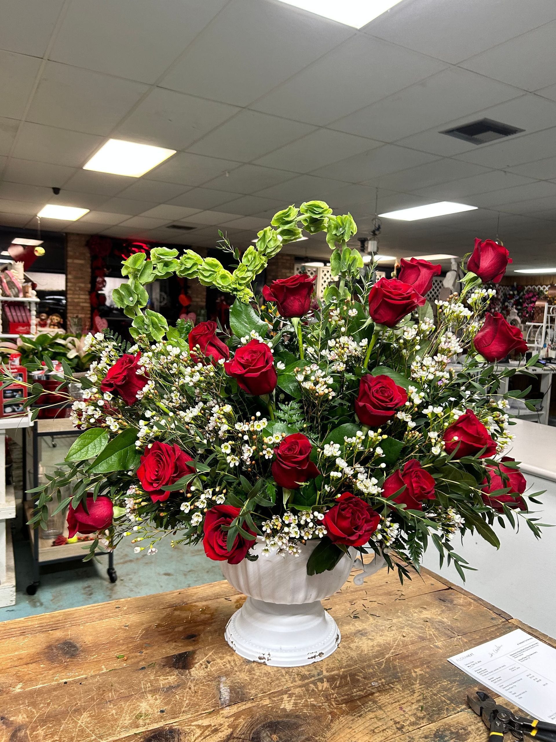 A vase filled with red roses and greenery is sitting on a wooden table.
