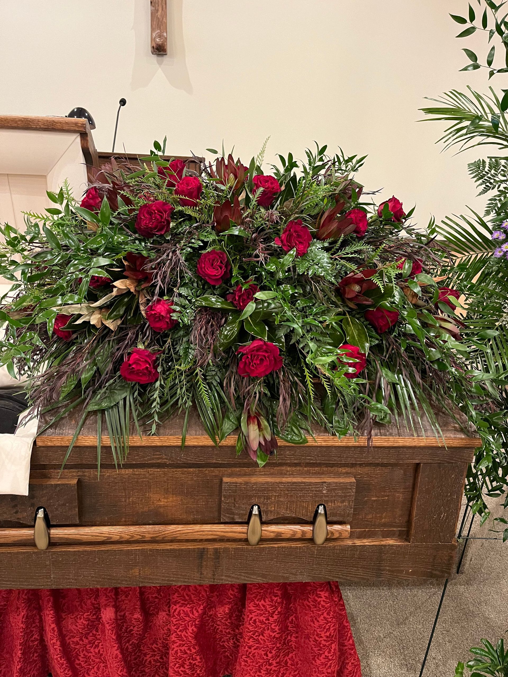 A wooden coffin decorated with red roses and greenery in a church.