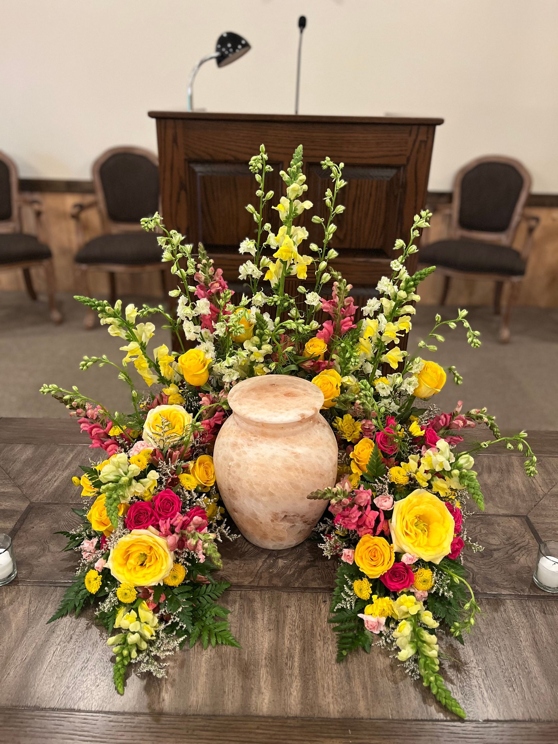 A urn is surrounded by flowers on a table in a church.