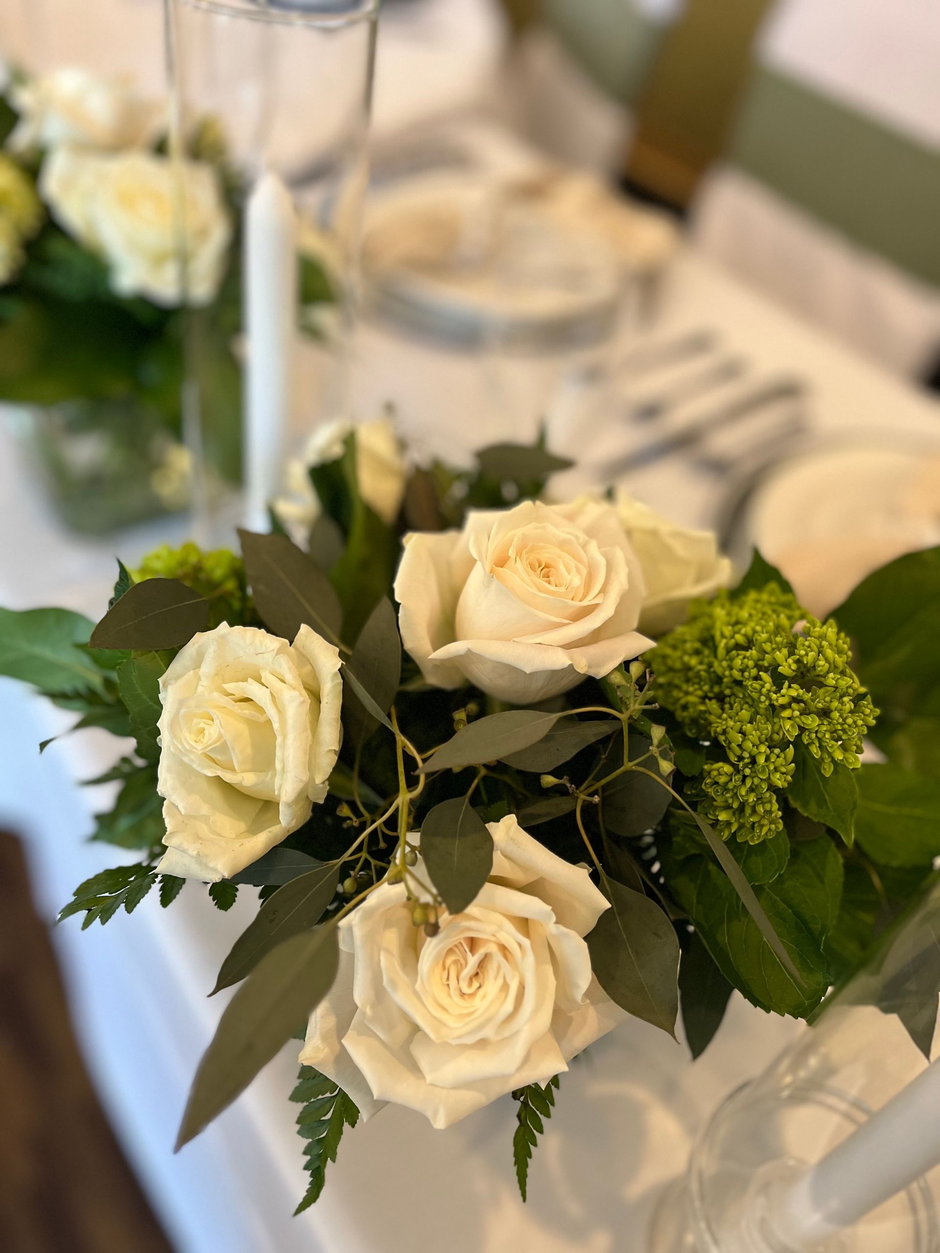 A table with white roses and green leaves on it.