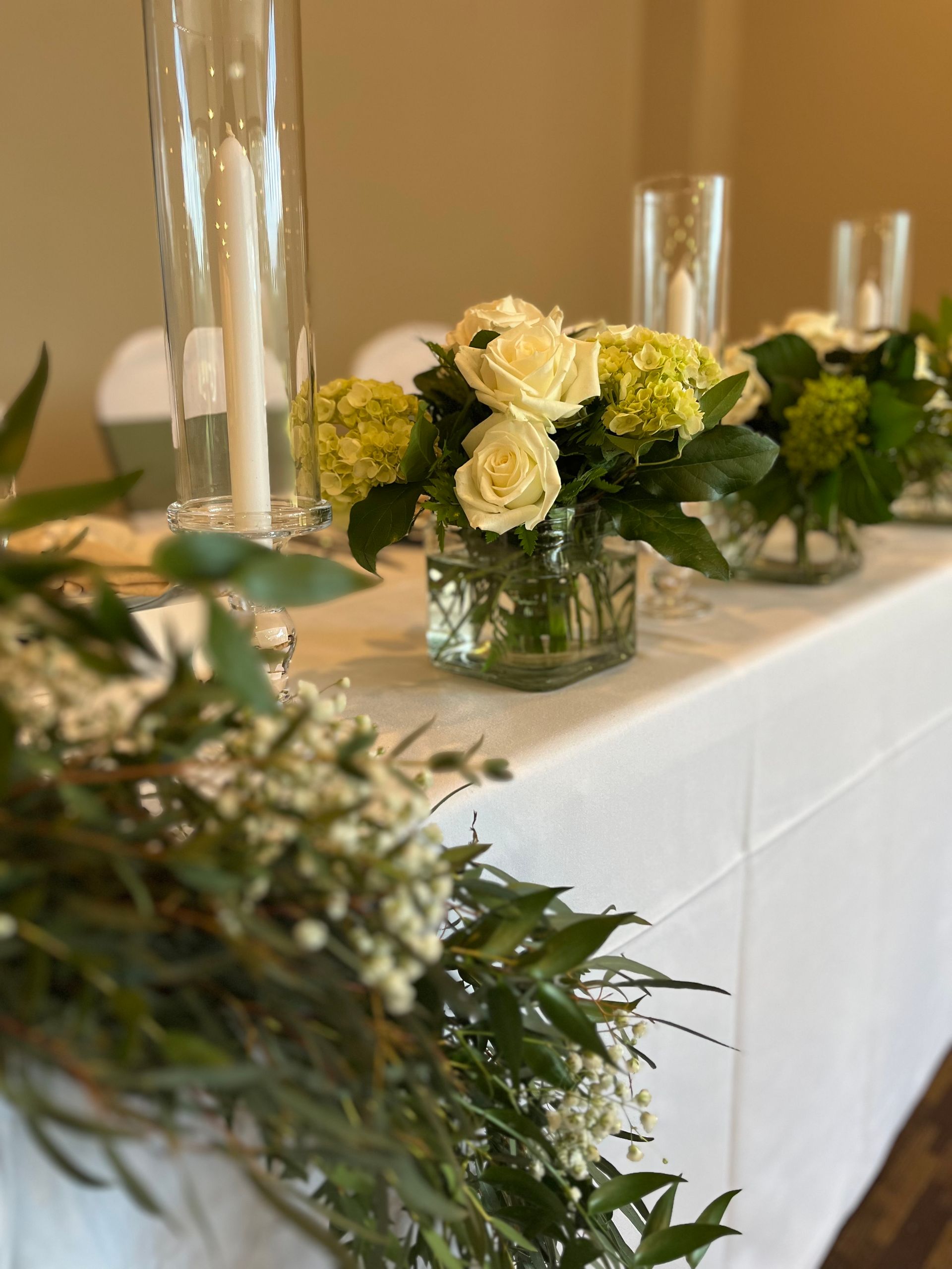 A long table with vases of flowers and candles on it.