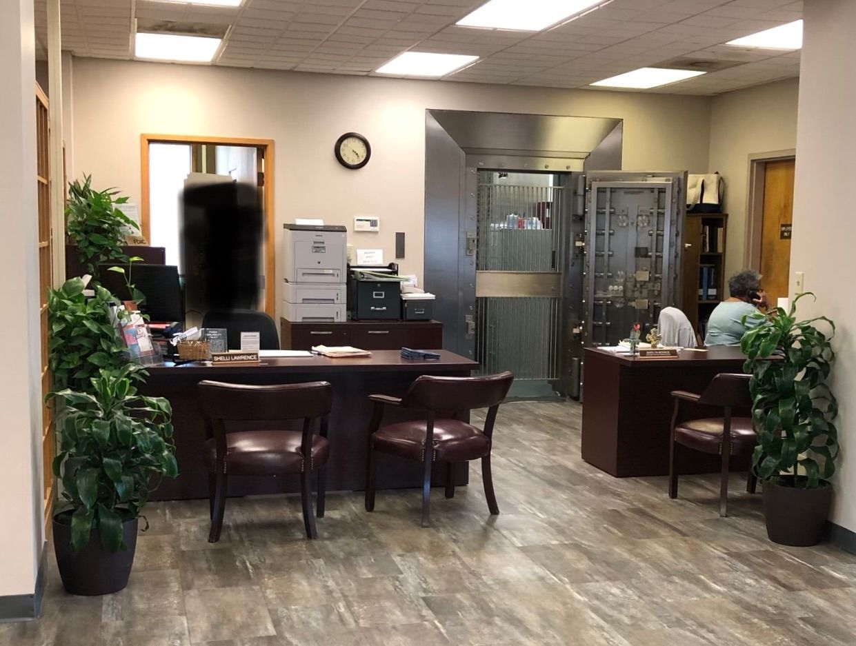 A man is sitting at a desk in a bank with a vault in the background.