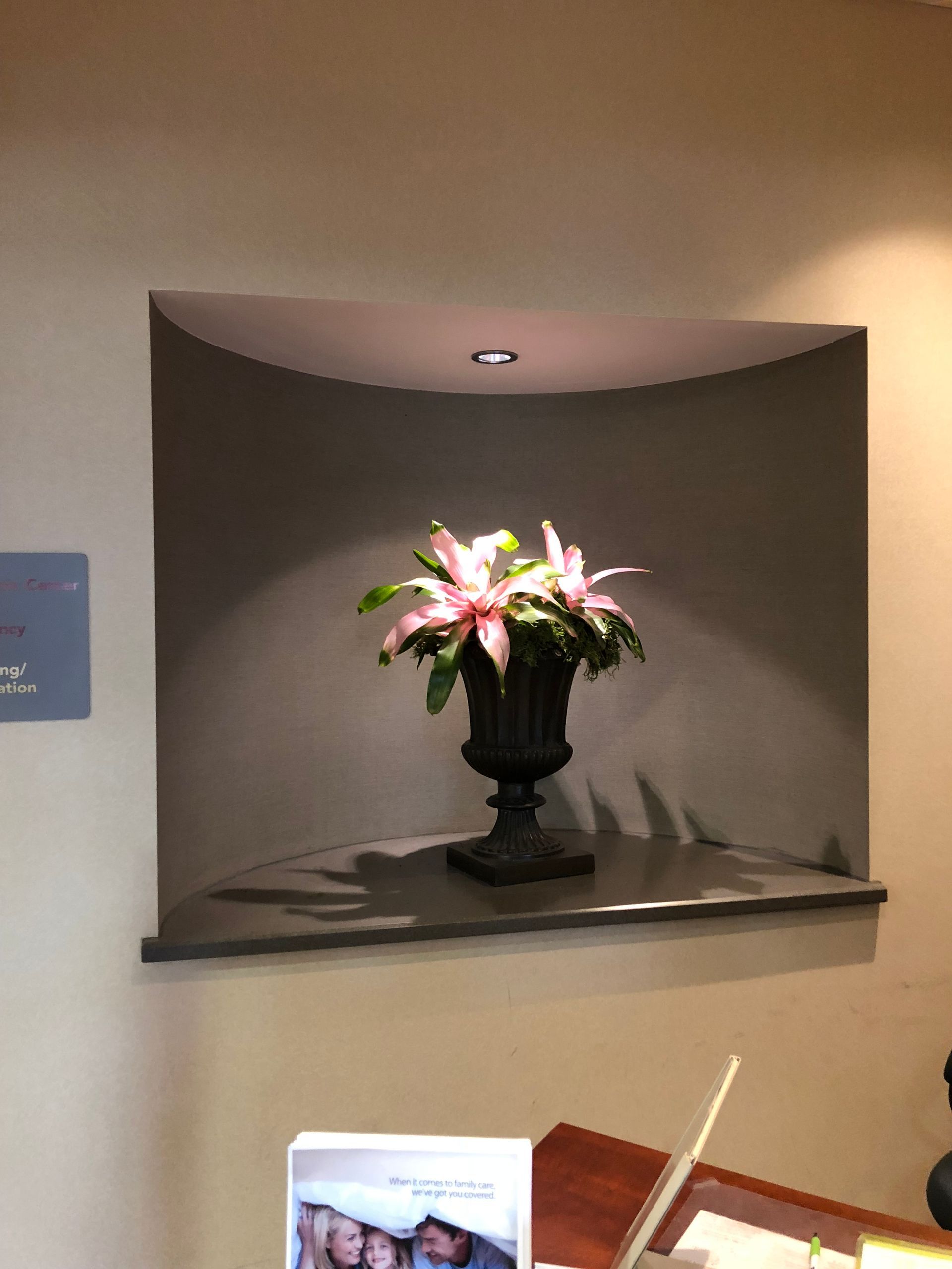 A vase of flowers is hanging on a wall above a desk.