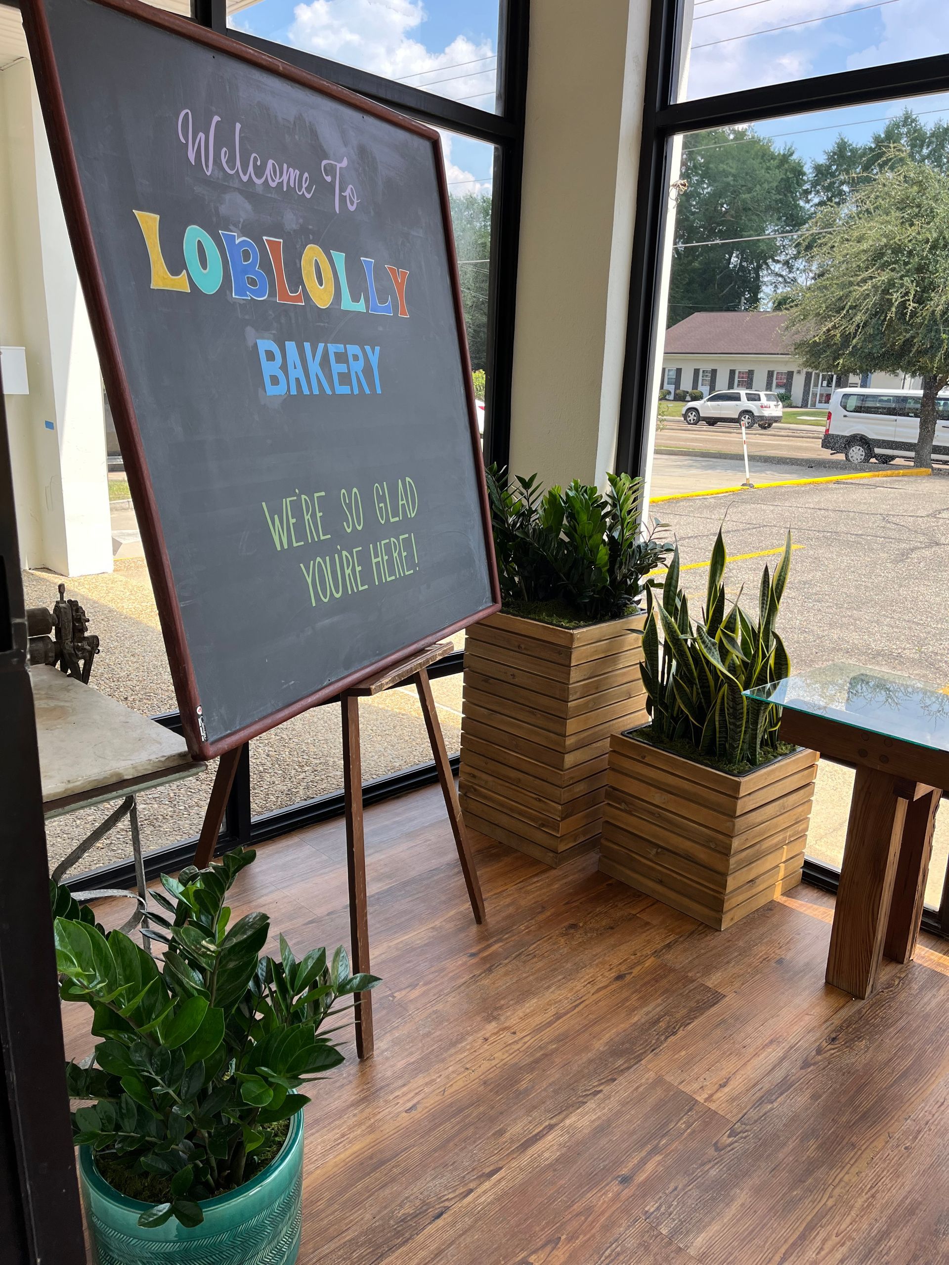 A chalkboard is sitting in front of a window in a bakery.