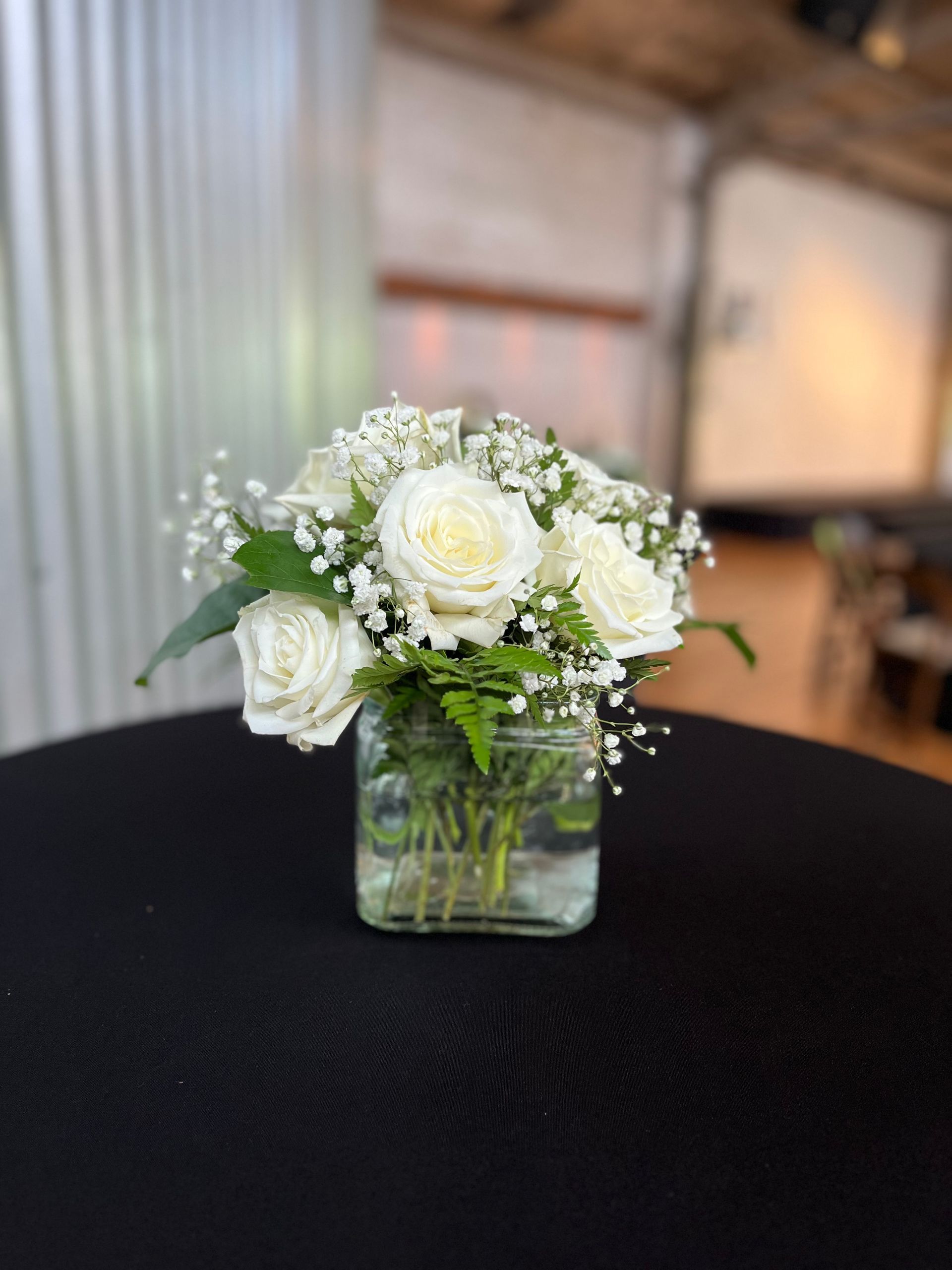 A vase filled with white roses and baby 's breath is on a table.