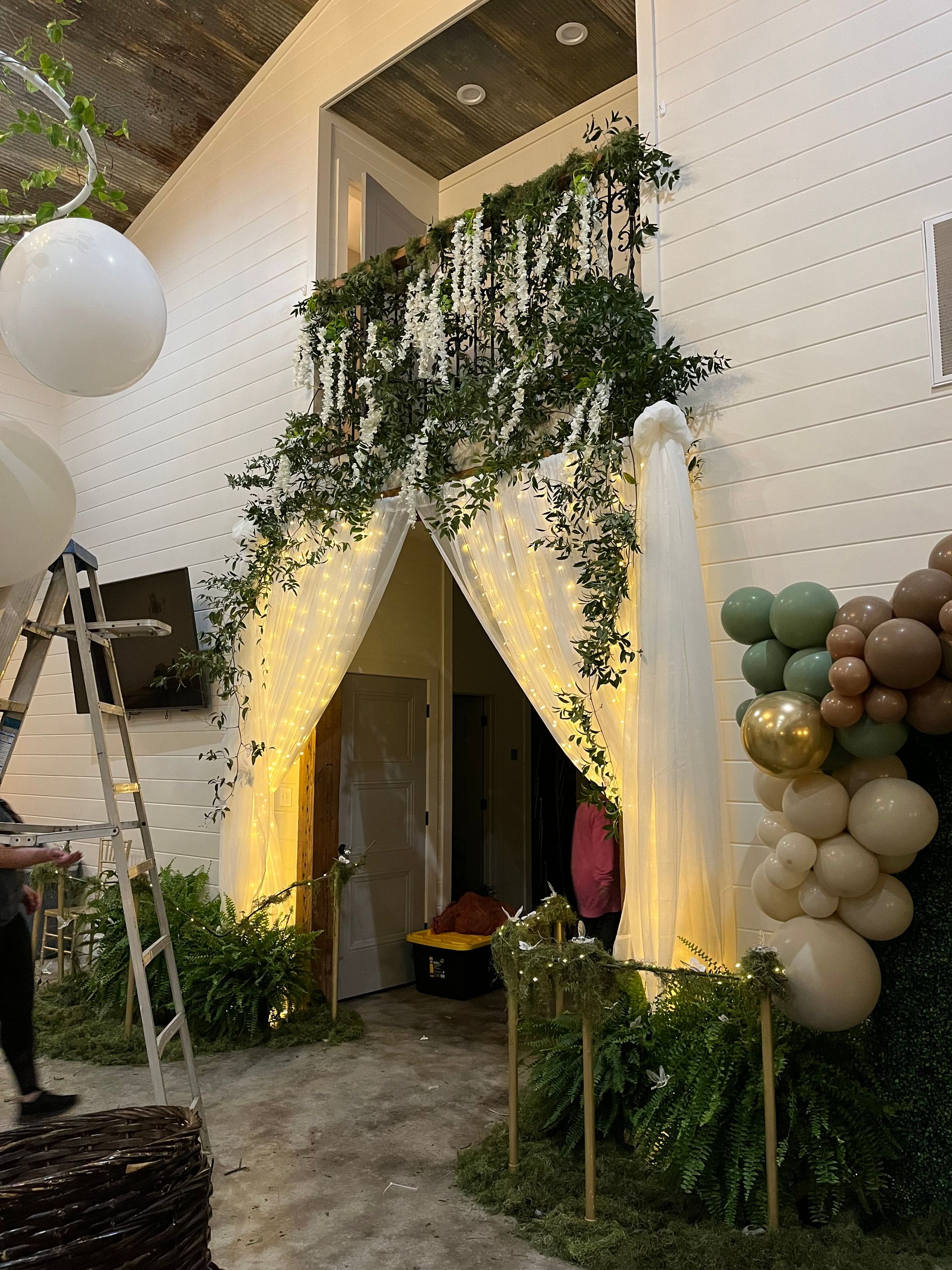 A man is standing next to a ladder in a room with balloons and flowers.