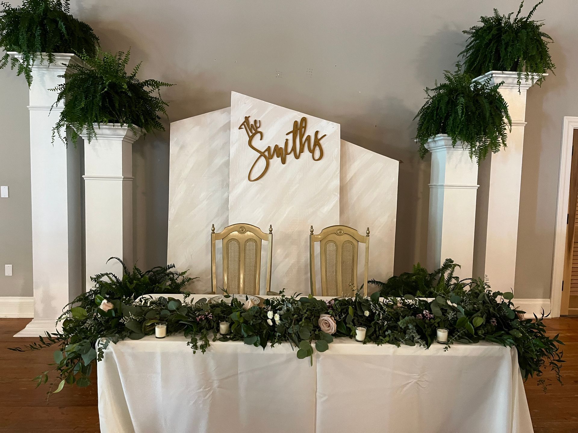 A table with a white table cloth and chairs in front of a wall with the name smiths on it.