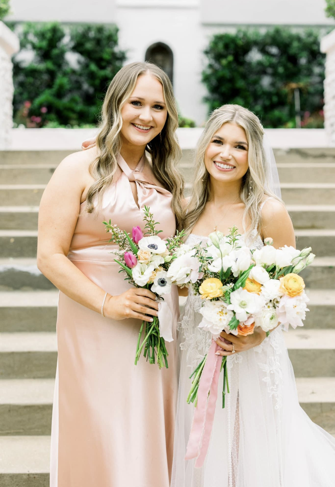 A bride and her bridesmaid are posing for a picture on a set of stairs.