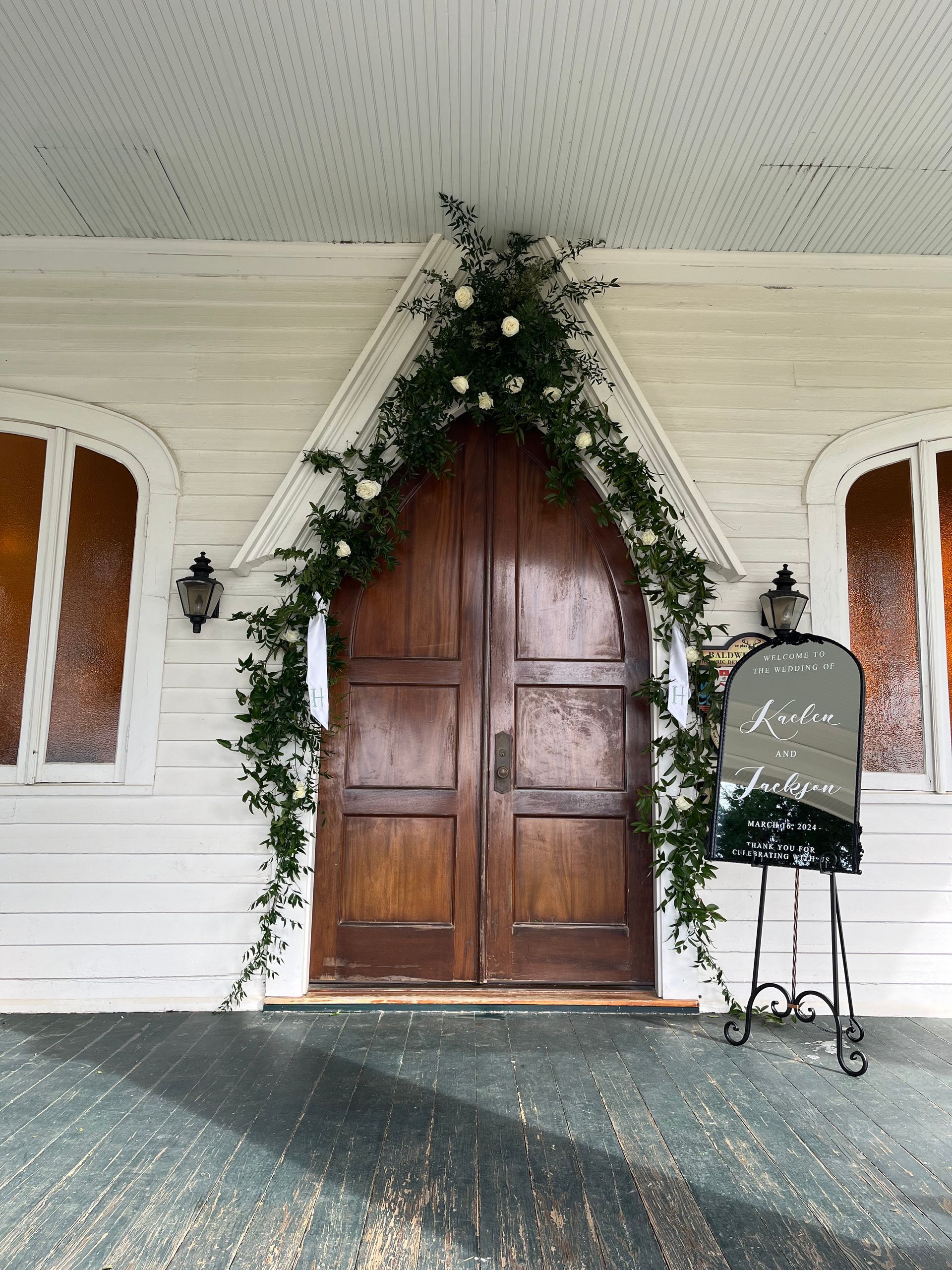 The front door of a church is decorated with flowers and greenery.