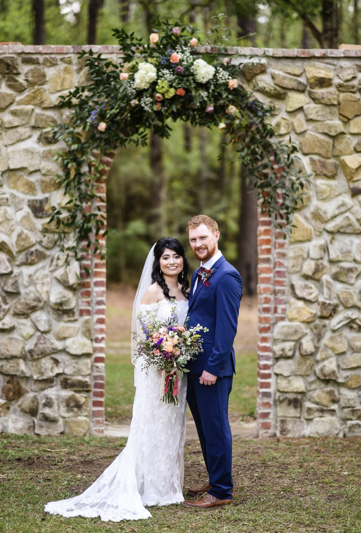 A bride and groom are posing for a picture in front of a stone arch.