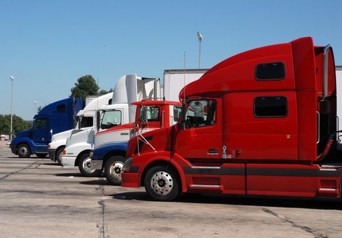Parked semi trucks in red, white, and blue lined up in a lot under a clear sky