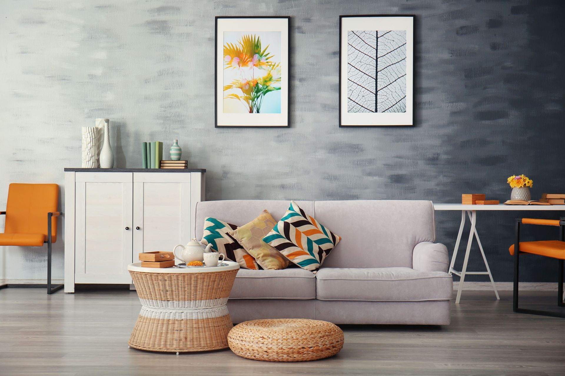 Modern living room with gray sofa, woven ottomans, framed wall art, and an orange chair by a white cabinet