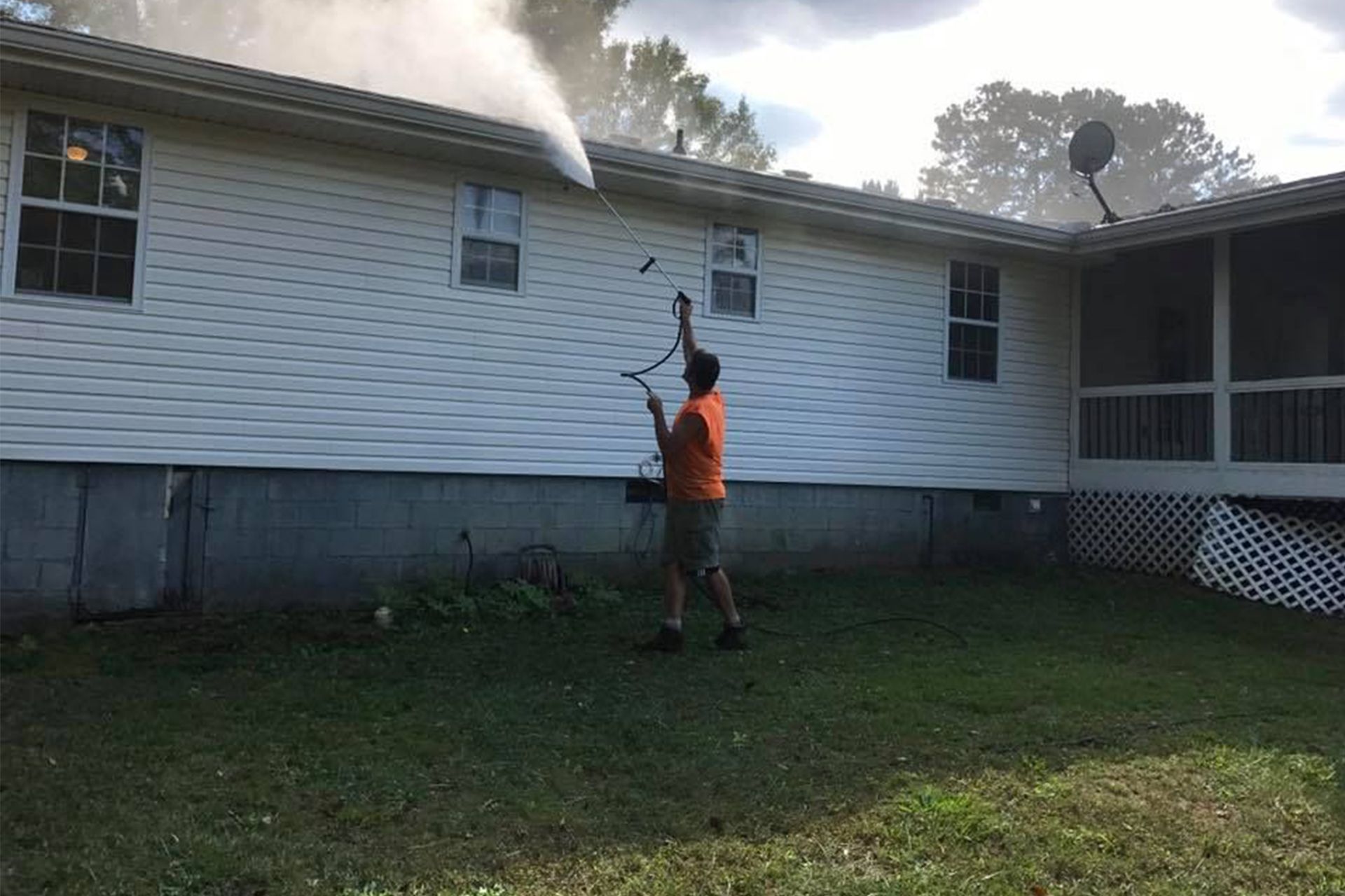 Person spraying water at smoke near a white house with a screened porch and satellite dish