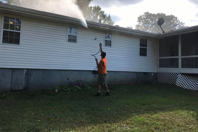 Person spraying water at smoke near a white house with a screened porch and satellite dish