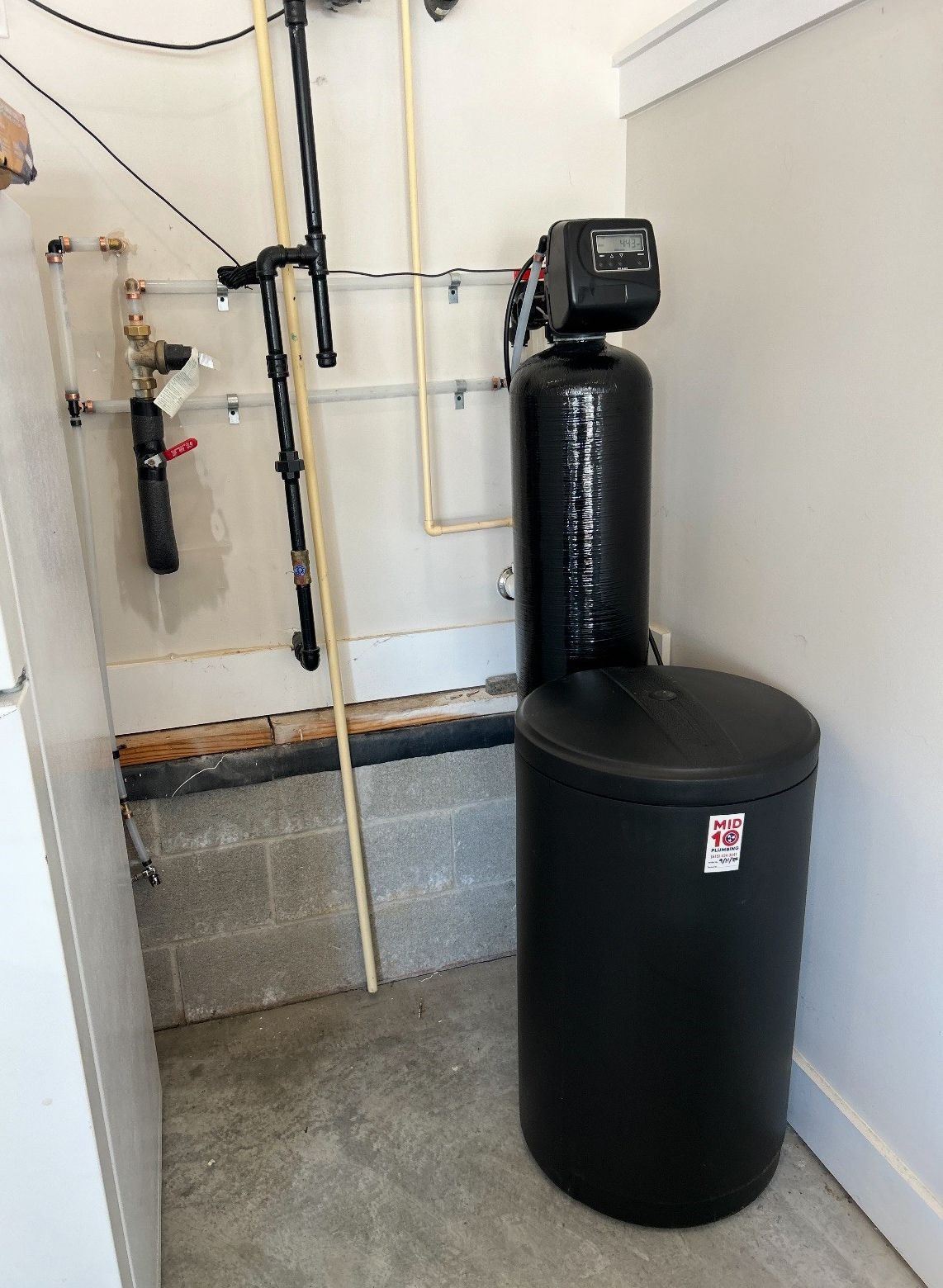 A black water softener is sitting in a corner of a garage.