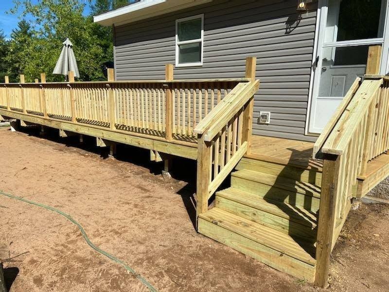 Wooden deck with stairs beside a gray house, overlooking a sandy yard.