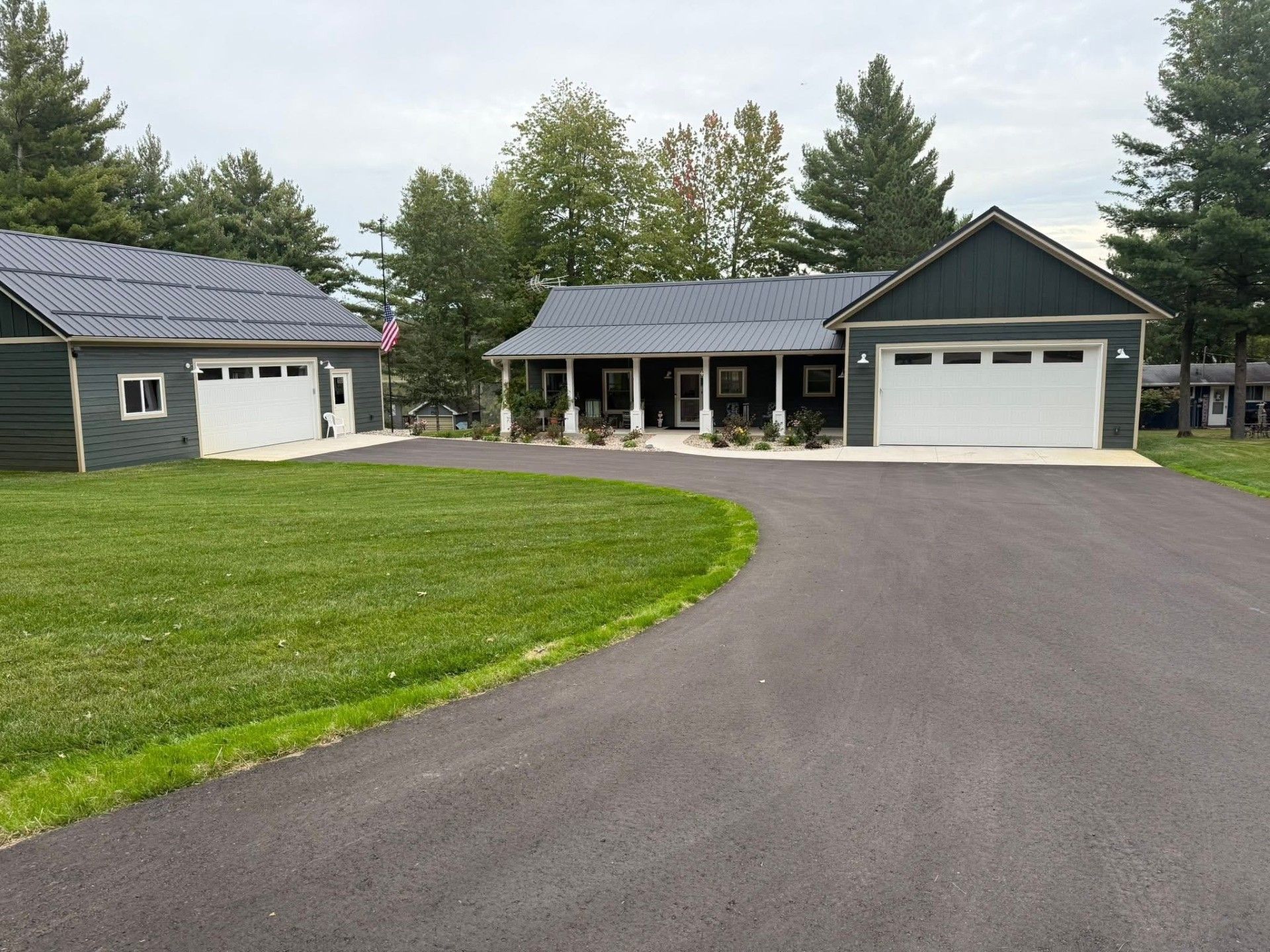 Suburban house with a curved driveway, green lawn, and two attached garages under a cloudy sky