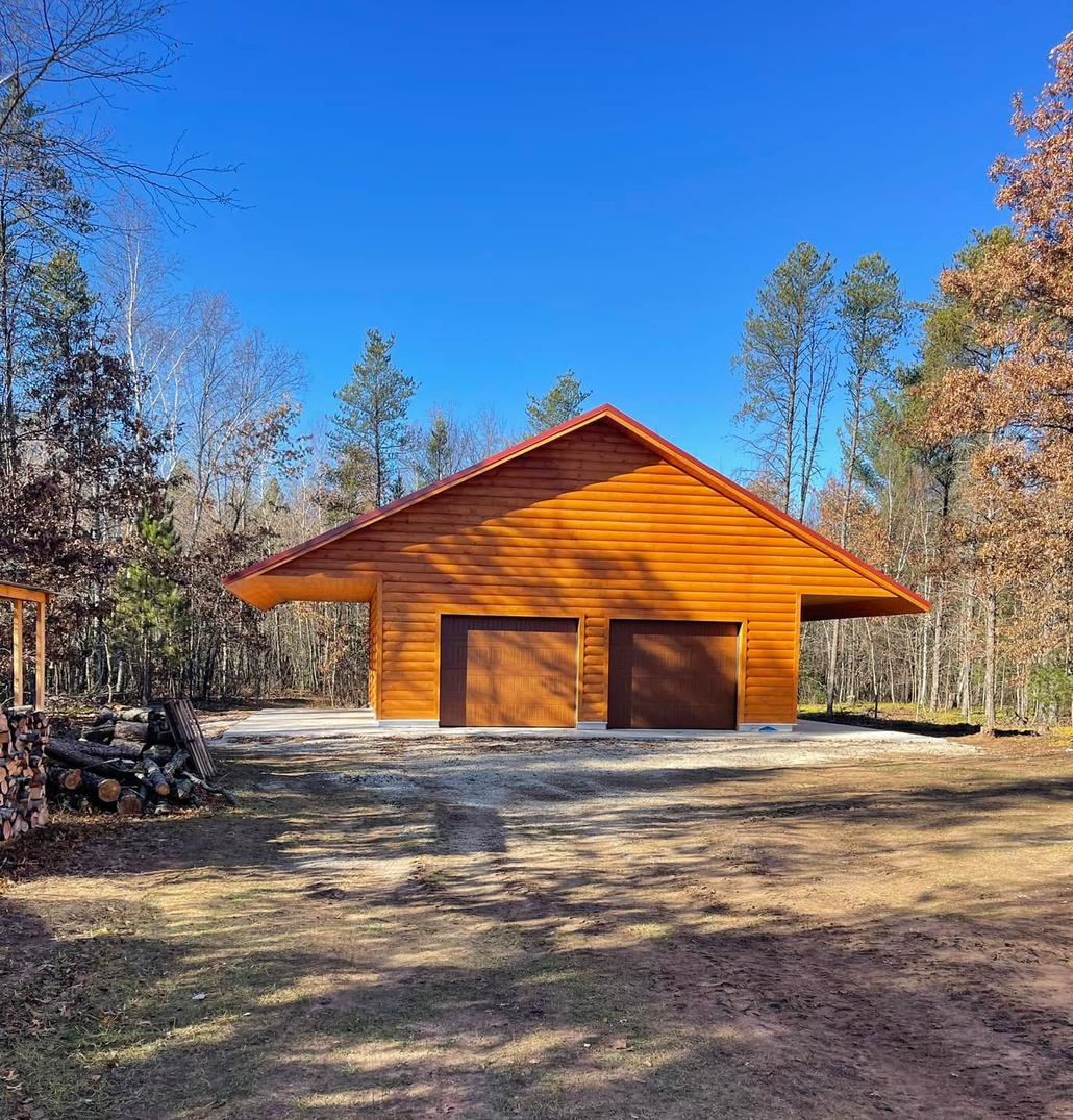 Wooden two-car garage in a wooded yard under a clear blue sky