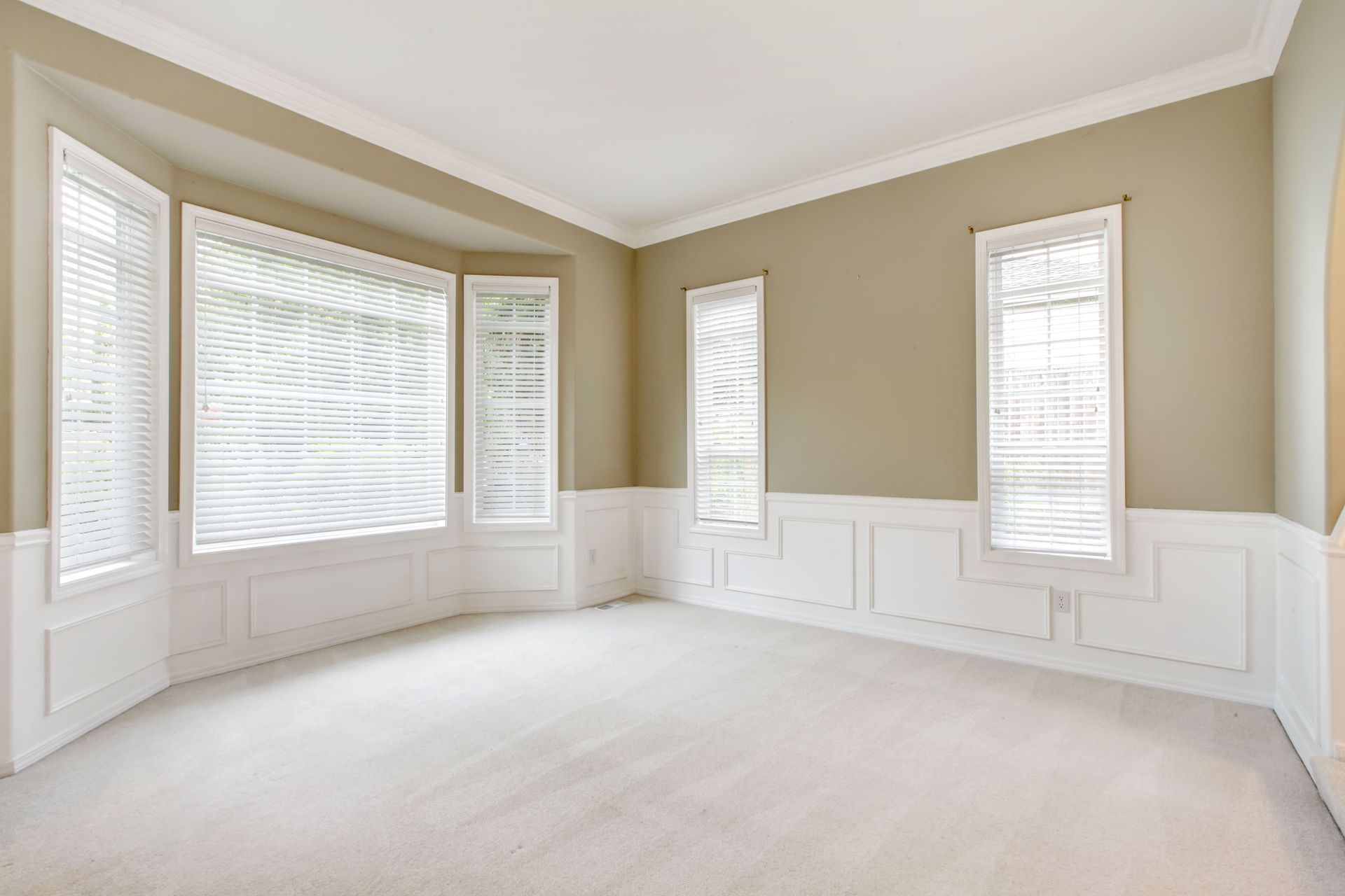 Empty room with beige walls, white trim, three windows with blinds, and light carpet.