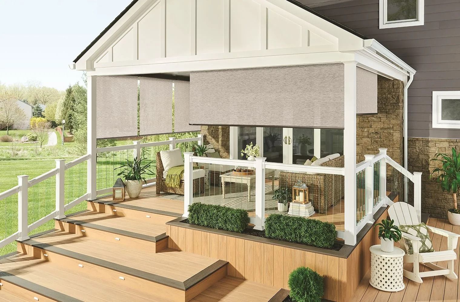 A covered porch with retractable blinds, outdoor furniture, and greenery.