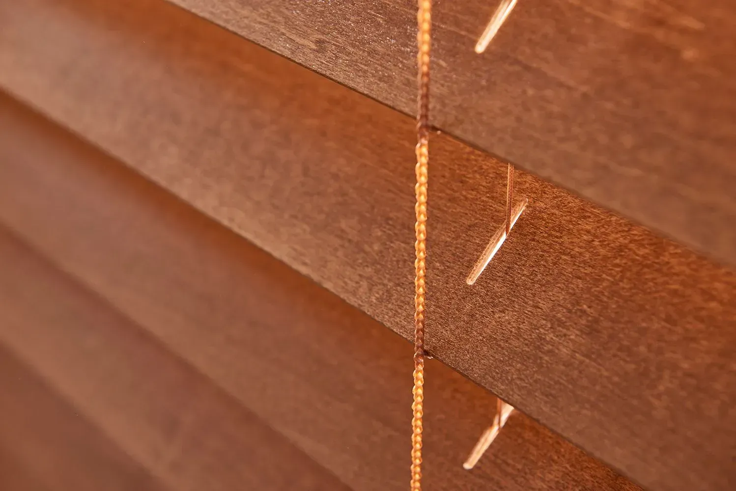 Close-up of wooden blinds, warm brown color, with a vertical cord running through slats.